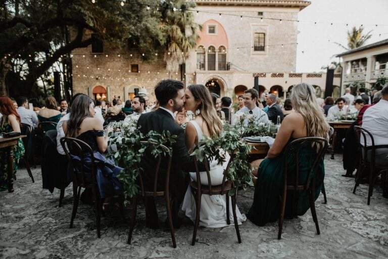 A bride and groom share a kiss as they sit at their wedding reception.