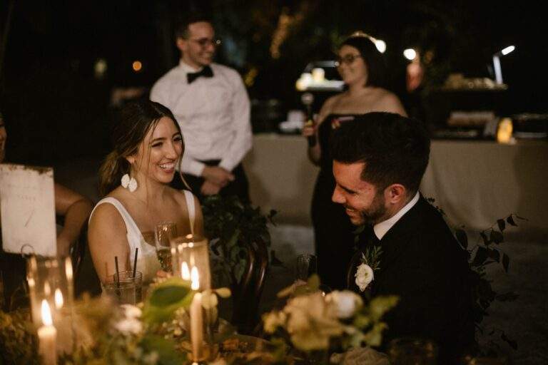 A bride and groom laughing together as they sit at their wedding reception.