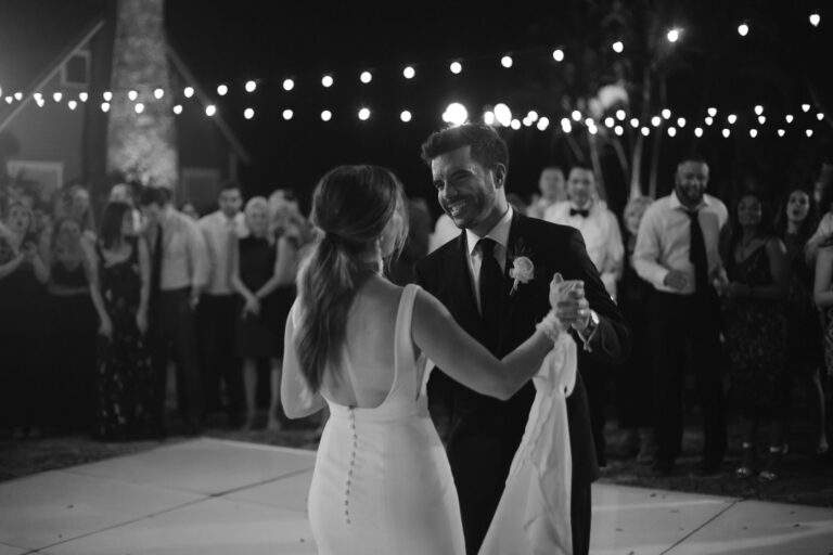 In black and white, a bride and groom dance slowly and closely together at their wedding reception.