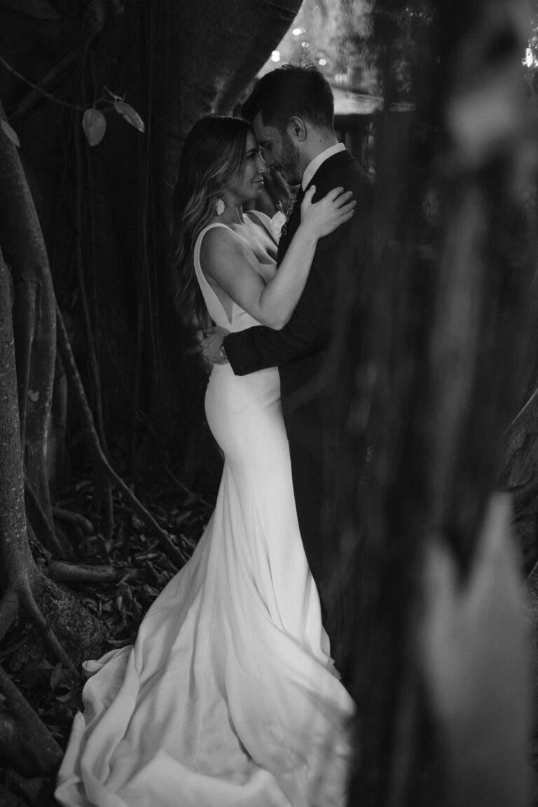 In black and white, a bride and groom hold each other close as they pose for a photo.