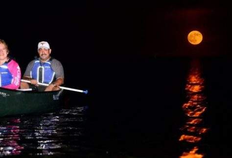 Two people in a canoe on Biscayne Bay at night with the full moon shining above them.